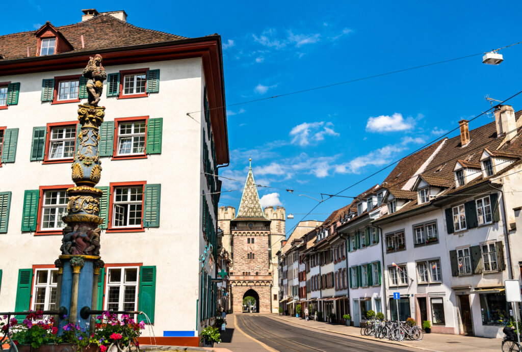 Spalentor in Basel mit Brunnen und Altstadthäusern an einer Tramstraße bei blauem Himmel