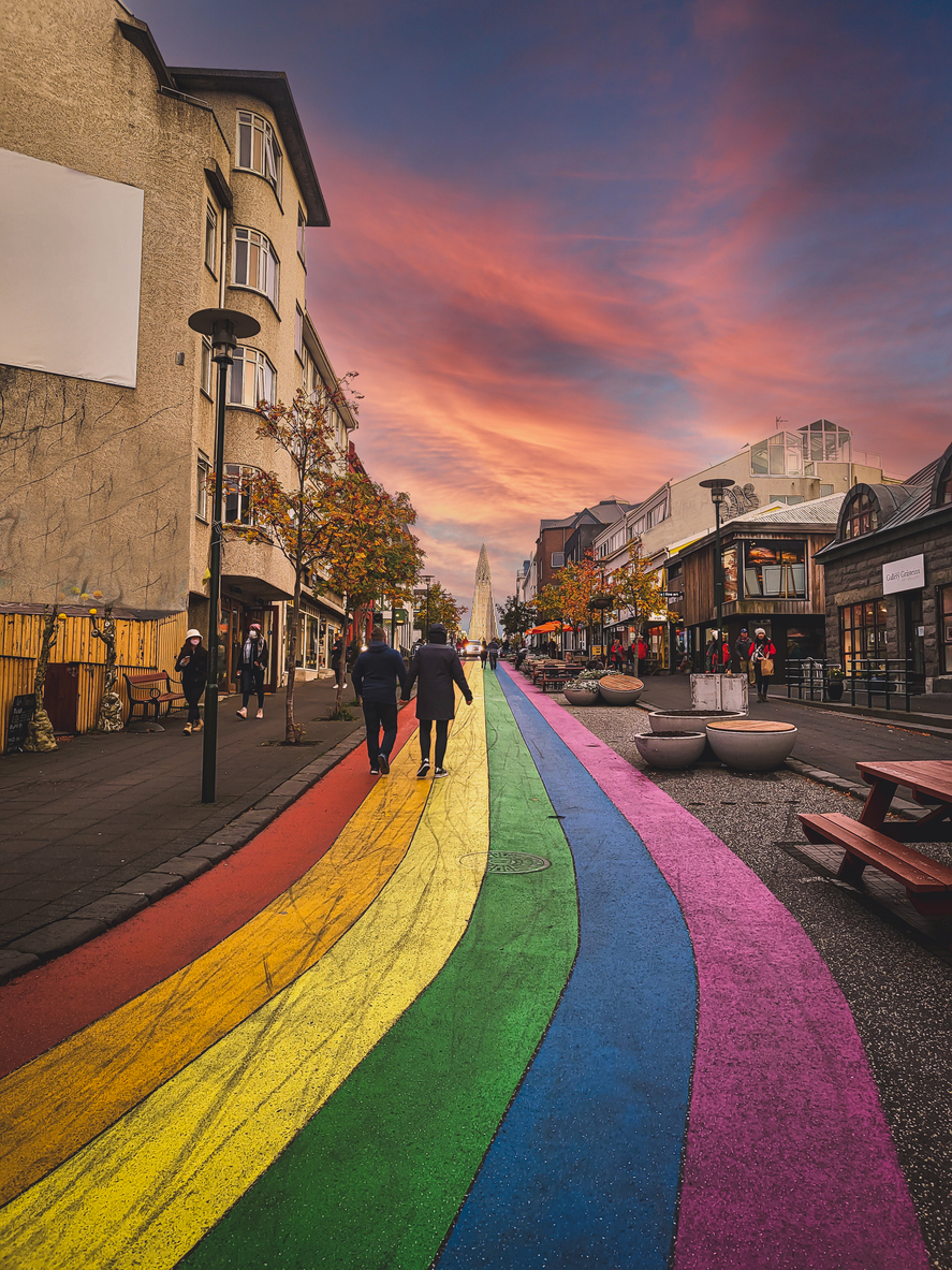 Bunte Regenbogenstraße in Reykjavik, die direkt auf die Hallgrimskirkja-Kirche zuläuft, bei Sonnenuntergang.