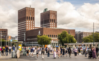 Menschen spazieren vor dem markanten Rathaus von Oslo mit seinen zwei Türmen.