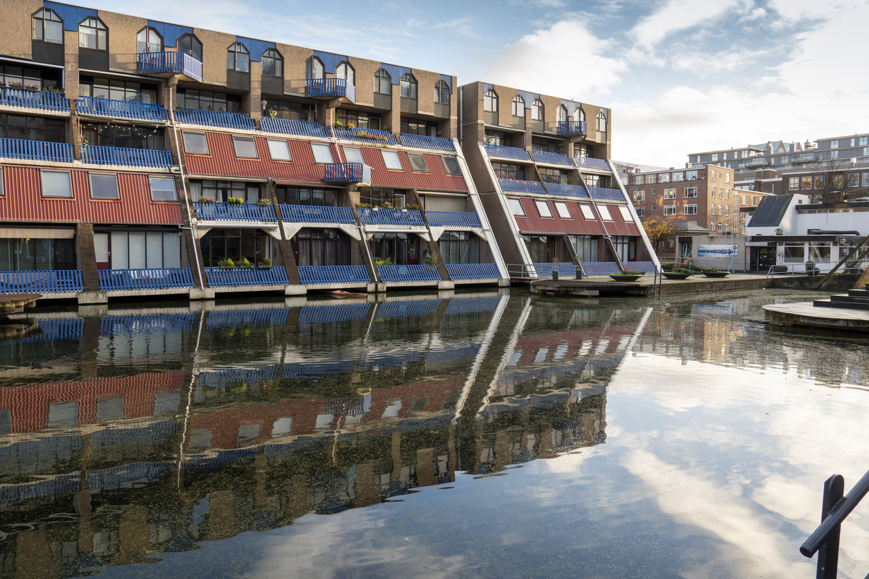 Moderne terrassenartige Wohnblöcke mit blauen Balkonen, Spiegelung im Kanal in Rotterdam.