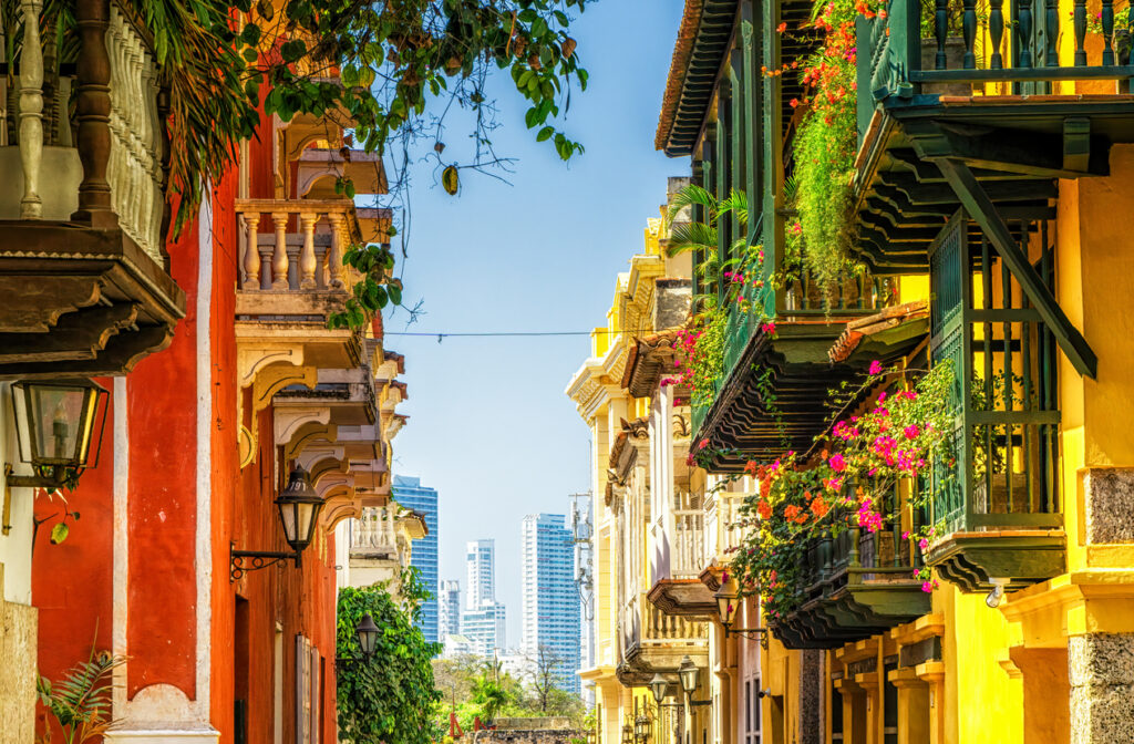 Bunte Kolonialhäuser mit Blumenbalkonen in der Altstadt von Cartagena, dahinter moderne Skyline.