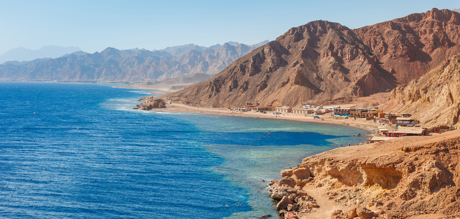 Küste von Dahab mit Bergen, türkisfarbenem Meer und kleinen Tauchbasen am Ufer.