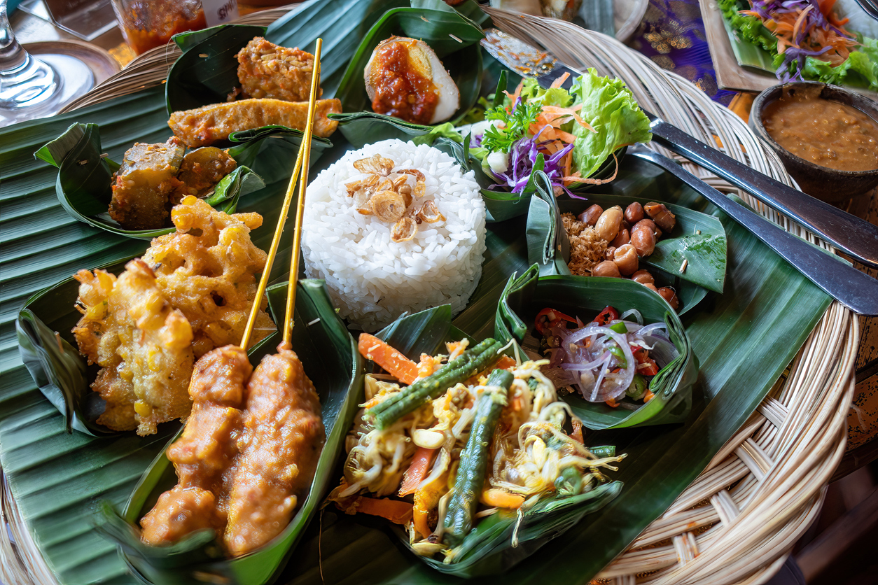 Balinesischer Nasi-Campur-Teller auf Bananenblättern mit Reis, Satay, Gemüse, Sambal und Beilagen