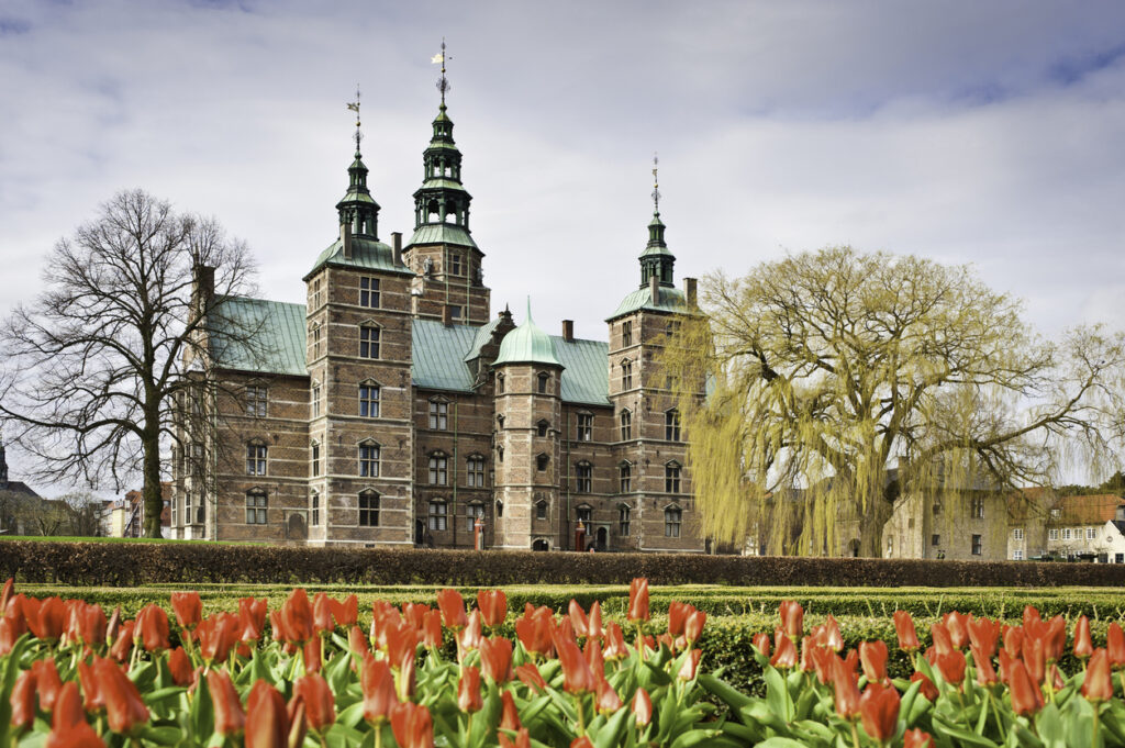 Blick auf Schloss Rosenborg in Kopenhagen mit blühenden roten Tulpen im Vordergrund und historischem Bauwerk im Hintergrund.