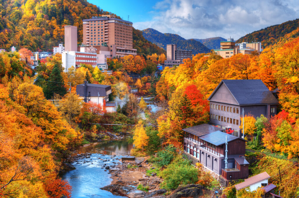 Fluss in einem bunt verfärbten Herbsttal mit Onsen-Gebäuden in Hokkaidō