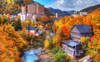 Fluss in einem bunt verfärbten Herbsttal mit Onsen-Gebäuden in Hokkaidō