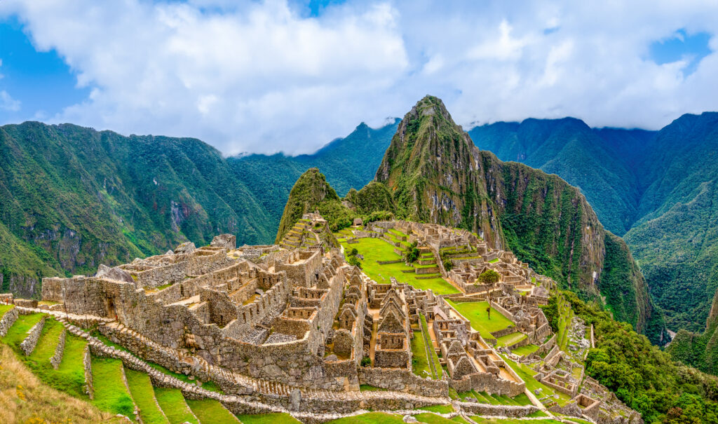 Panorama von Machu Picchu mit Terrassen und Steinruinen; Huayna Picchu dahinter, Wolken.