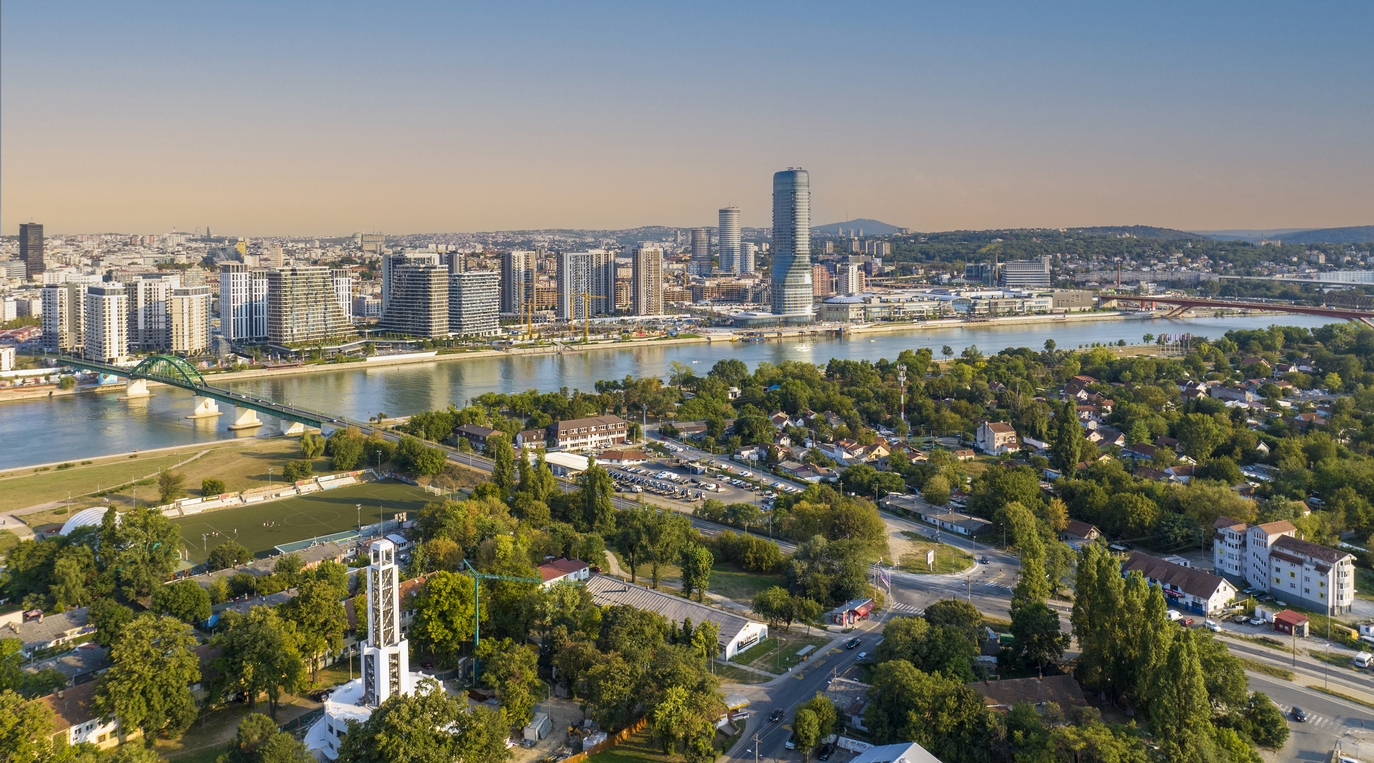 Belgrad, Panorama entlang der Sava mit geschwungenem Hochhaus Kula Belgrade und Wohntürmen der Belgrade Waterfront, Alte Sava-Brücke links, Vorstadtviertel und Uferparks im Vordergrund, klarer Himmel