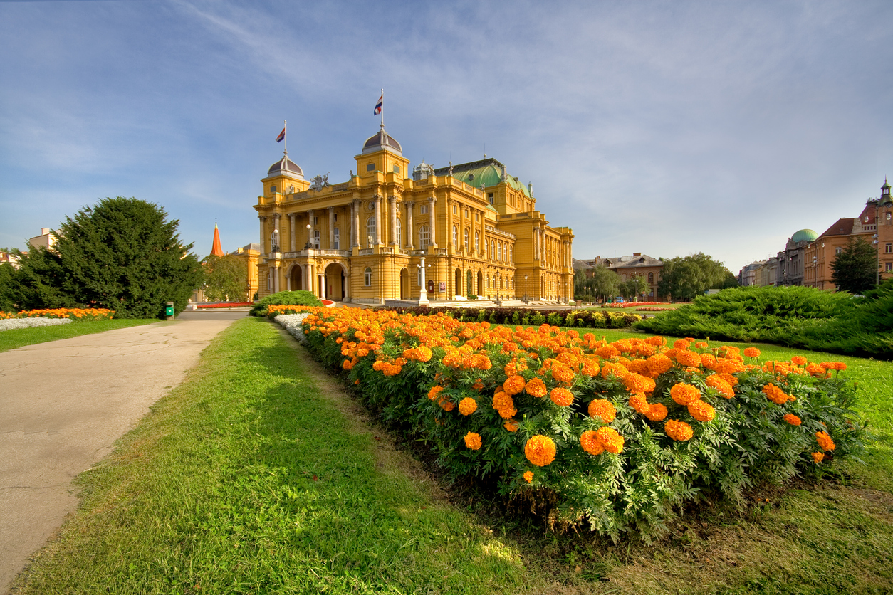 Das Kroatische Nationaltheater in Zagreb mit blühenden Blumenbeeten im Vordergrund.