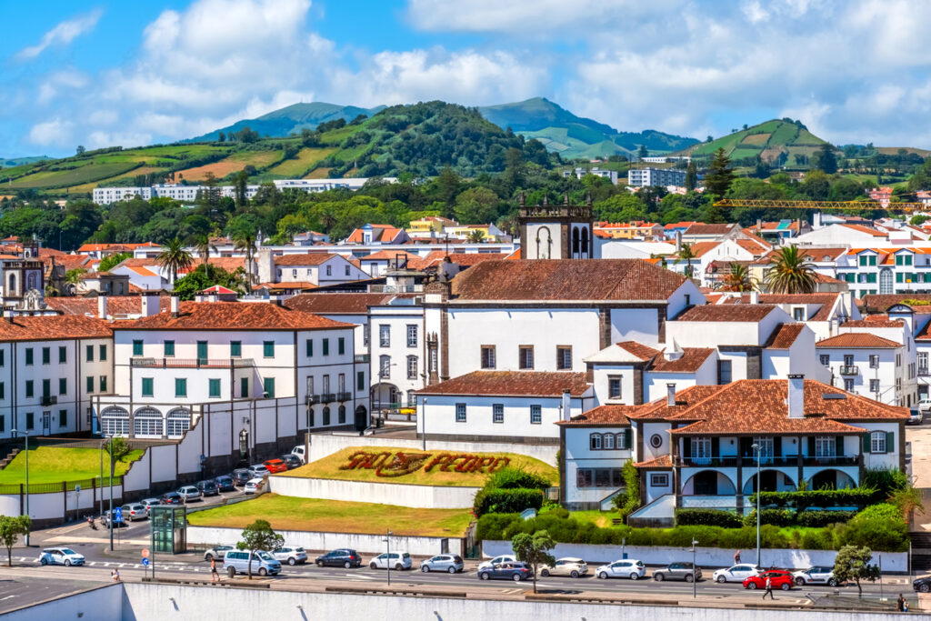Ponta Delgada auf São Miguel mit weißen Häusern, rotem Ziegeldach, Kirchturm und grünen Hügeln im Hintergrund