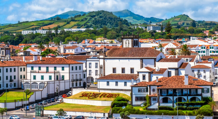 Ponta Delgada auf São Miguel mit weißen Häusern, rotem Ziegeldach, Kirchturm und grünen Hügeln im Hintergrund