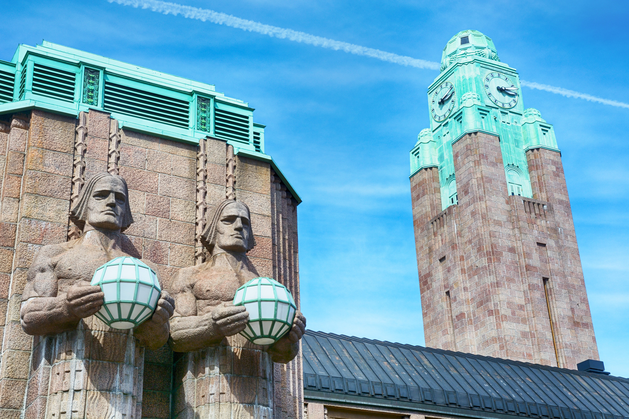 Detailansicht des Hauptbahnhofs von Helsinki mit markanten Granitstatuen und Uhrturm.