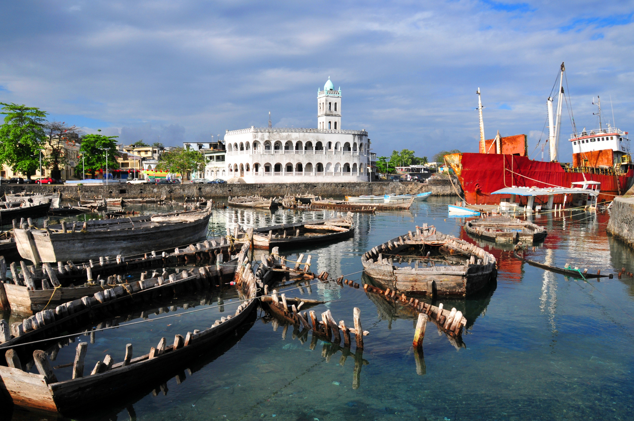 Historischer Hafen auf den Komoren mit weißen Arkadenbau und vielen Holzbooten im Wasser.