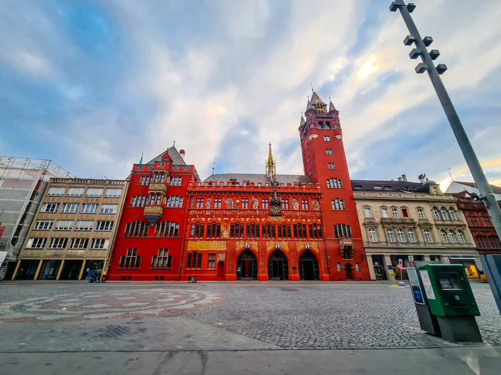 Basler Rathaus mit roter Fassade und Turm am Marktplatz, umgeben von Häuserzeile und weitem Platz