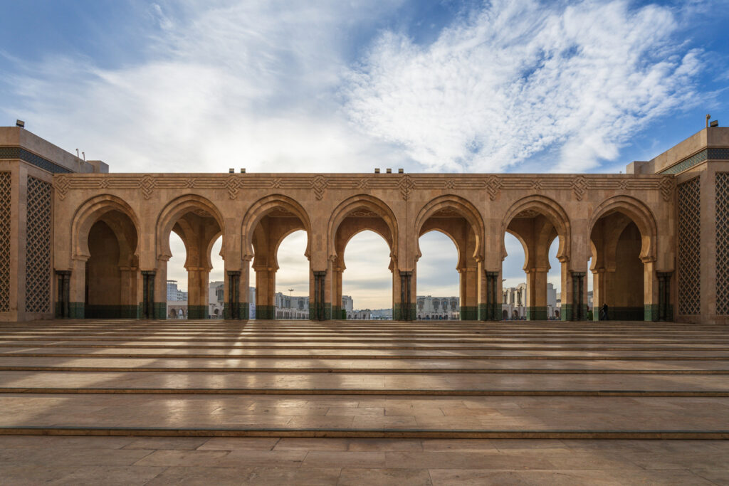Arkadengang der Hassan-II.-Moschee in Casablanca mit Hufeisenbögen und Steinplatten im Morgenlicht.