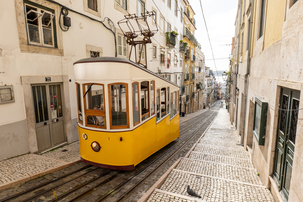 Gelbe Standseilbahn „Elevador da Bica“ fährt durch eine steile Kopfsteinpflastergasse in Lissabon.