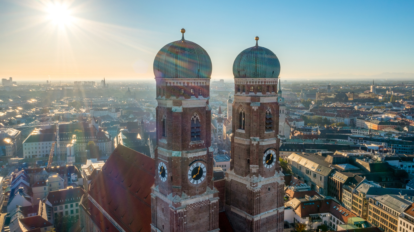 Luftaufnahme der Frauenkirche in München mit den markanten Zwiebeltürmen und Blick über die Stadt im Morgenlicht.