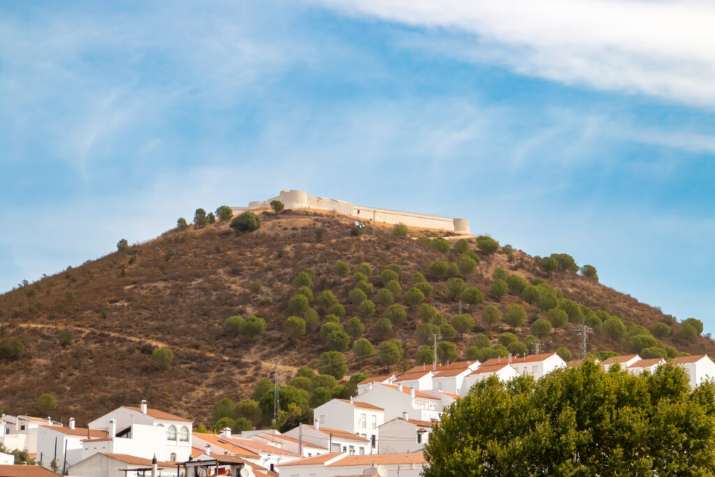 Festung auf Hügel über Sanlúcar de Guadiana mit weißen Häusern und blauem Himmel.