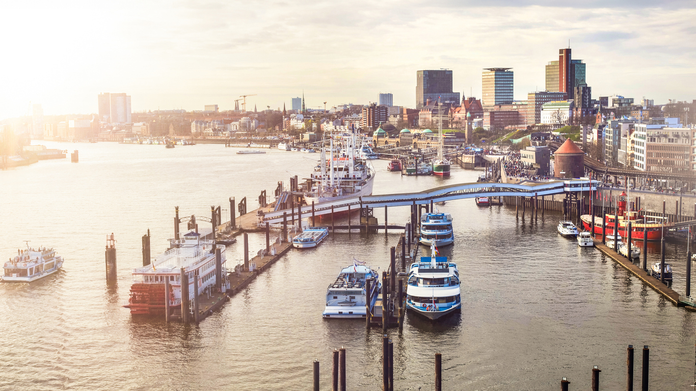 Hamburg, Panorama der Landungsbrücken mit Anlegern und Hafenfähren, vorn Cap San Diego, rechts Rickmer Rickmers und Kaimauern, Besucher auf der Promenade, warmes Gegenlicht über der Elbe