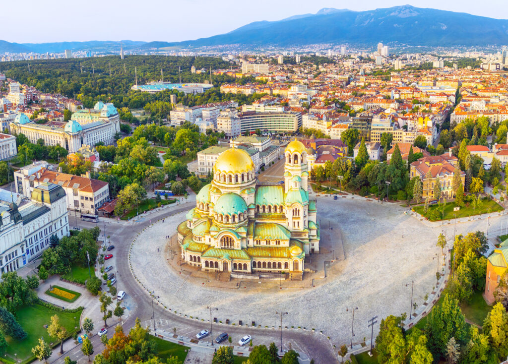 Sofia, Luftaufnahme der Alexander-Newski-Kathedrale mit goldenen Kuppeln und grünem Dach, weiter Rundplatz, umgebende Innenstadt, Vitosha-Gebirge im Hintergrund