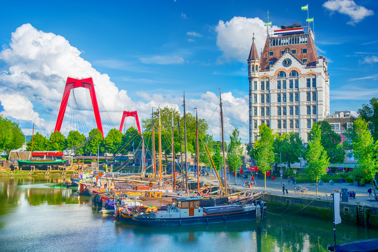 Historische Boote im Oude Haven, weißes Witte Huis und rote Willemsbrug bei blauem Himmel.