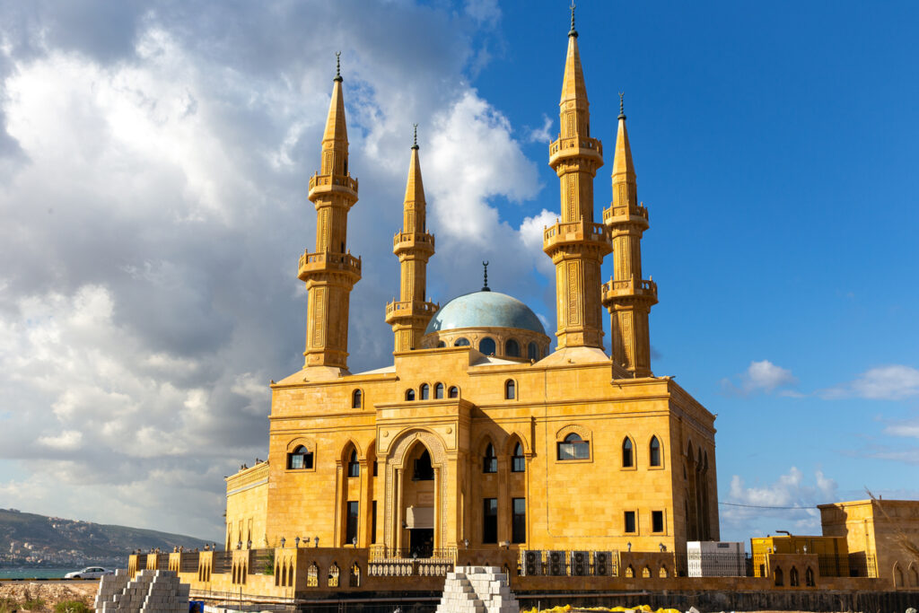 Goldfarbene Moschee mit blauer Kuppel und vier schlanken Minaretten vor blauem Himmel.