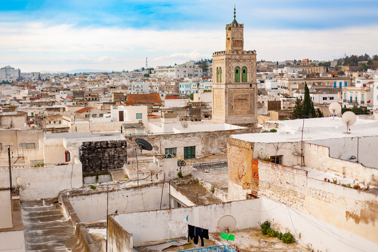 Panorama über die weißen Dächer der Medina von Tunis mit historischem Minarett, Satellitenschüsseln und blauem Himmel.