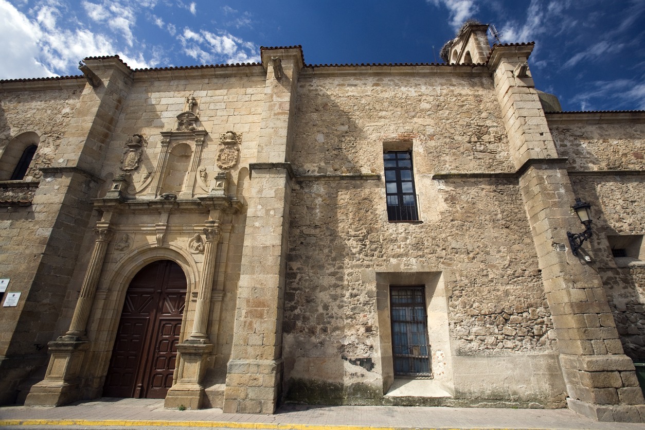 Steinernen Kirchenbau in Valencia de Alcántara mit dekoriertem Portal und blauem Himmel.