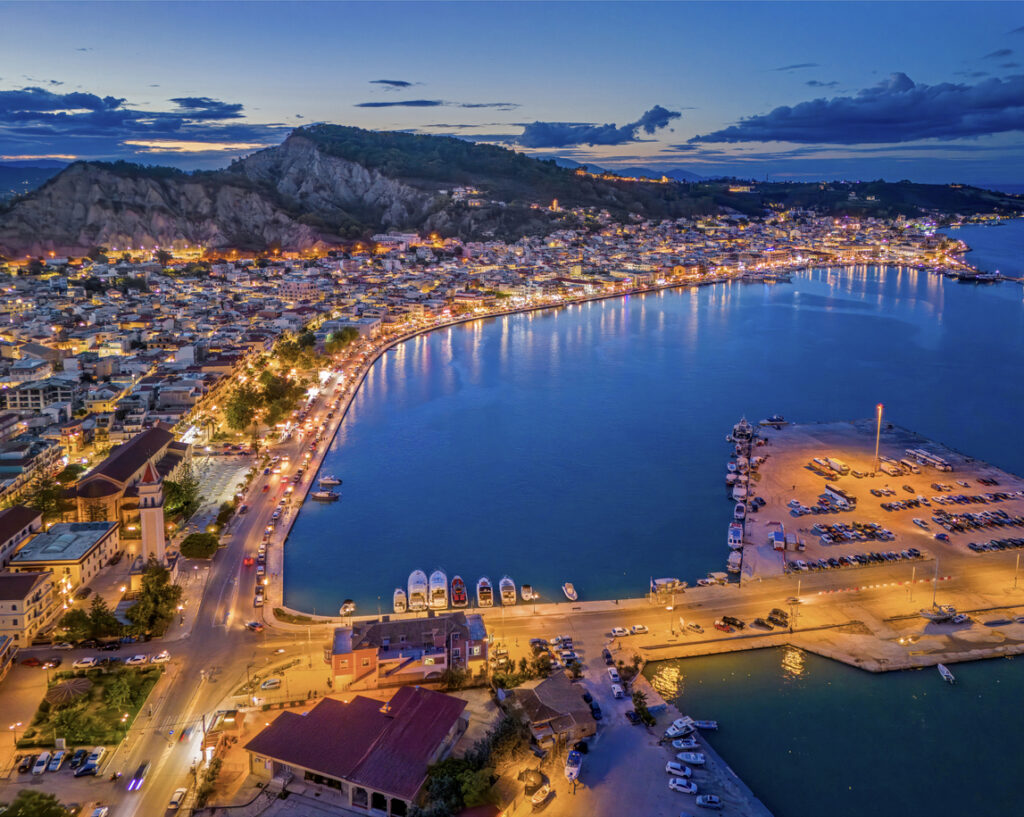 Abendliche Luftaufnahme von Zakynthos-Stadt mit beleuchteter Uferpromenade, Hafen und Booten.