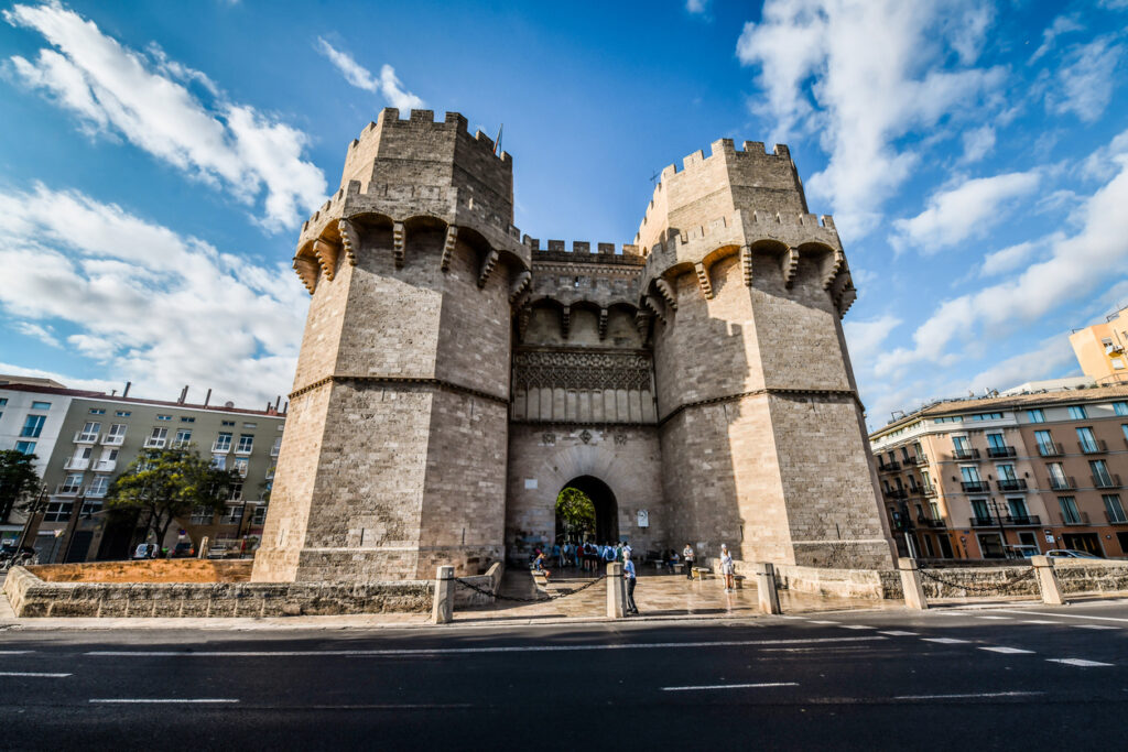 Frontalansicht der Torres de Serranos in Valencia, massives gotisches Stadttor mit zwei Türmen, Besucher am Eingang und blauer Himmel.