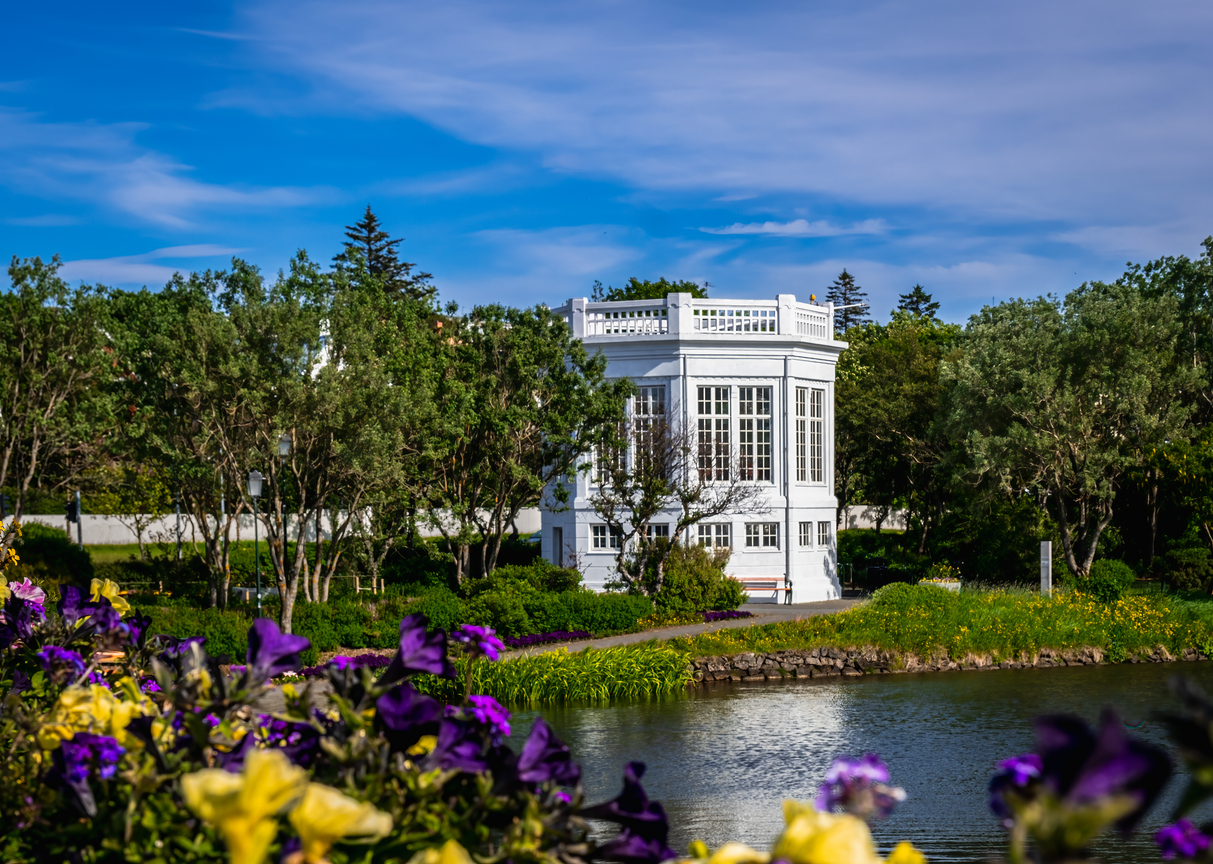 Weiße Parkvilla im Reykjavik Park, umgeben von Bäumen, Blumen und Teich.