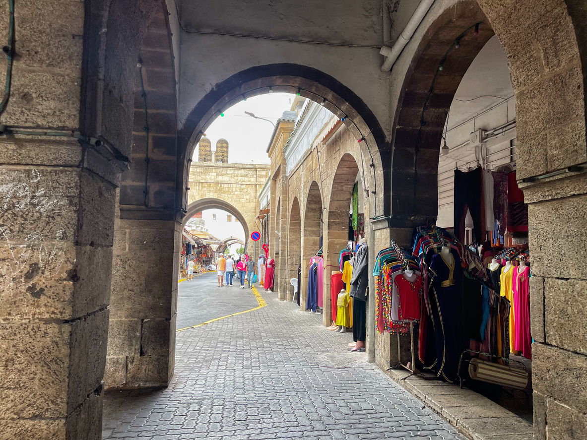 Steinarkaden mit Souk-Ständen in der Medina von Casablanca, bunte Kleidung und vorbeigehende Menschen.