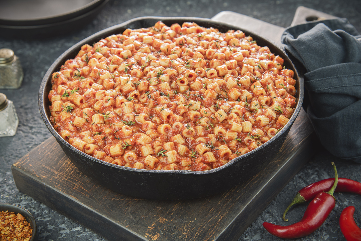 Pfanne mit Imbakbaka: kleine Pasta in kräftiger Tomatensauce, mit Kräutern; rote Chilischoten daneben.