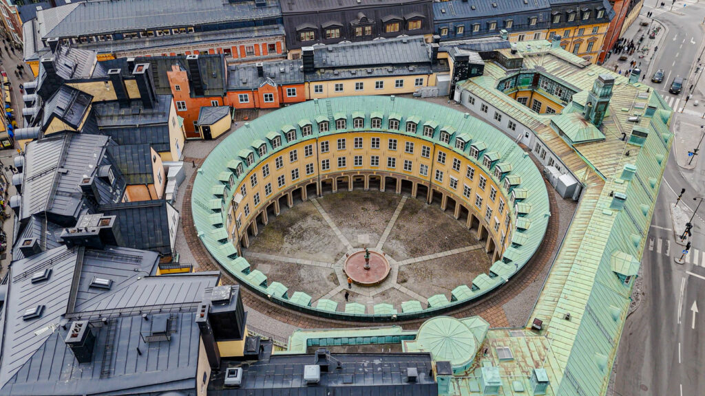 Stockholm, kreisförmiger Innenhof eines historischen Ringbaus, gelbe Fassaden, grüne Kupferdächer, zentrale Brunnenfigur, Luftaufnahme