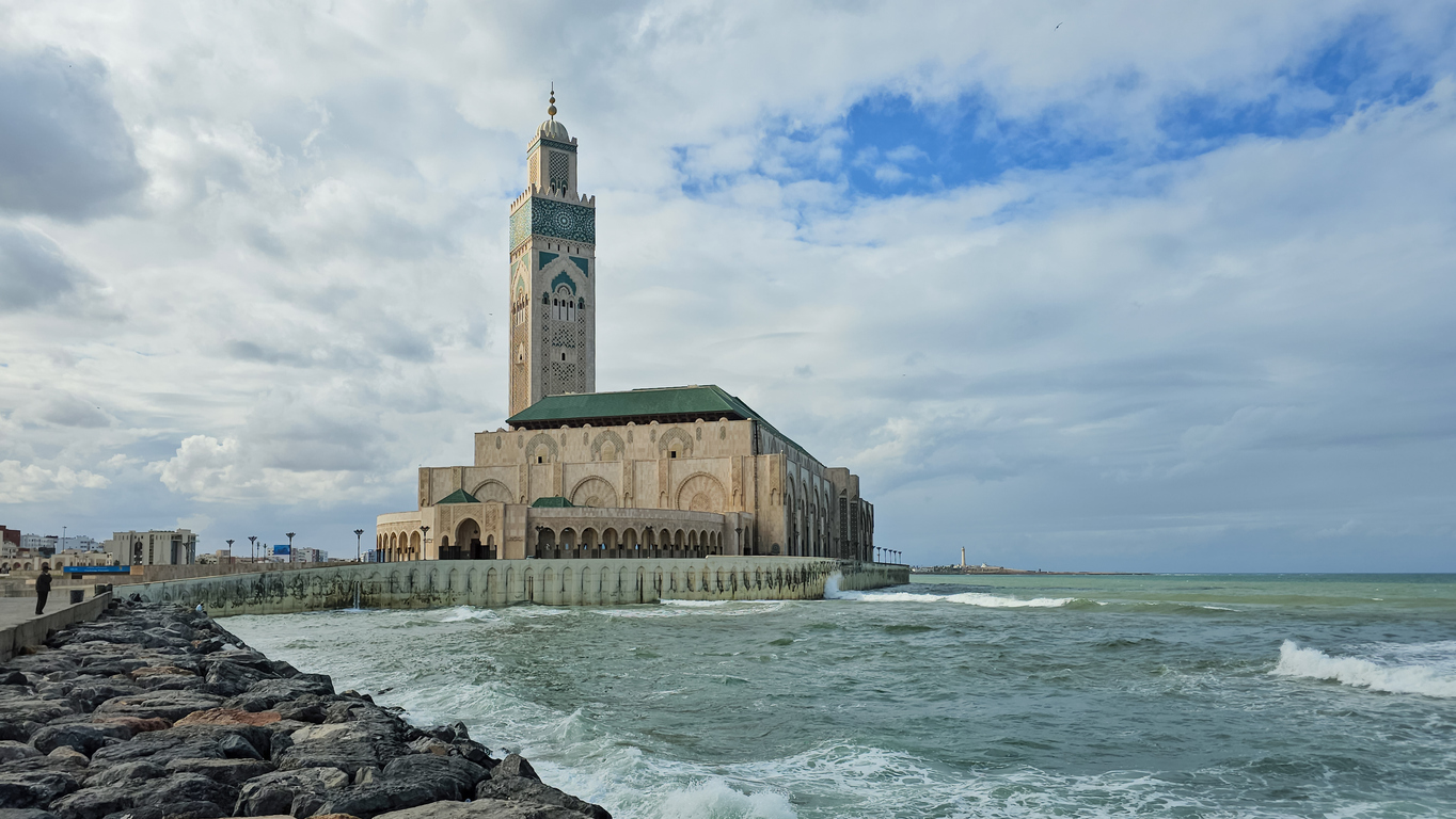 Hassan-II.-Moschee in Casablanca direkt am Meer mit Minarett, Wellen und Felswellenbrecher.