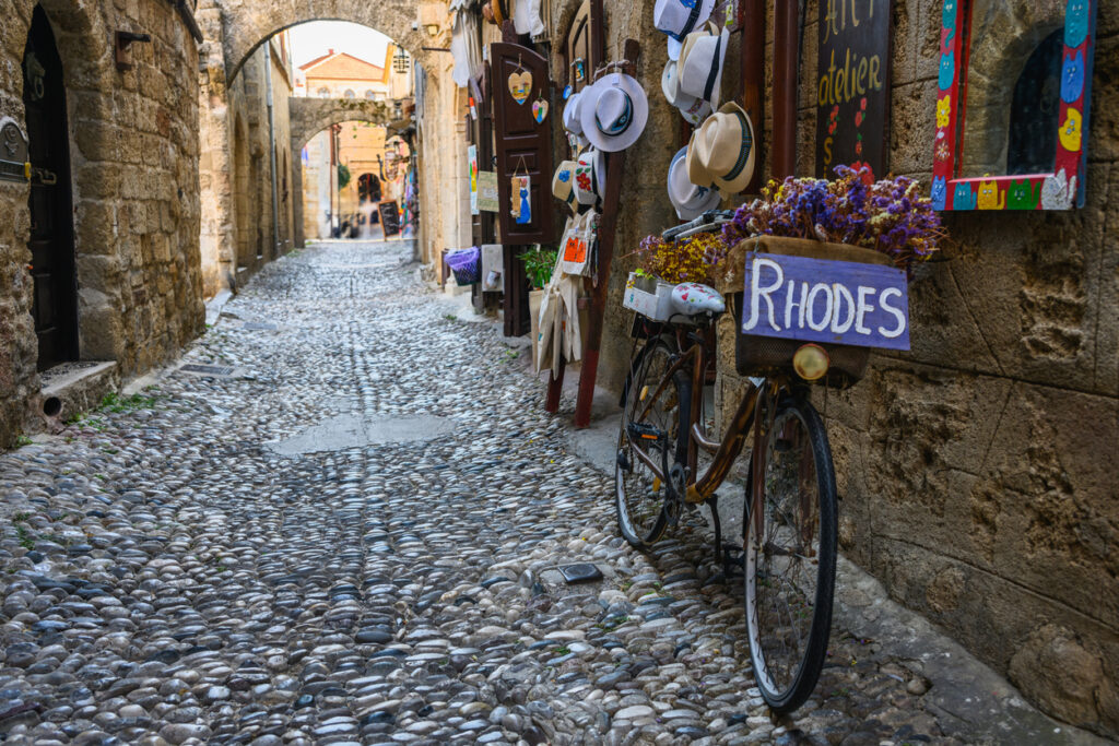 Kopfsteinpflaster-Gasse in der Altstadt von Rhodos mit Fahrrad, Steinbögen und Souvenirläden.