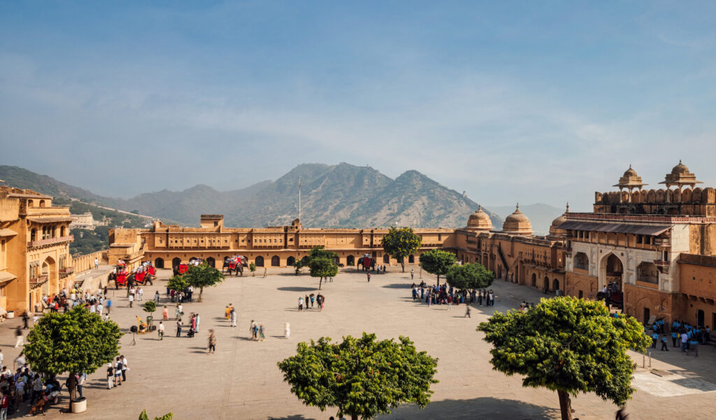Blick auf den Innenhof des Amber Fort in Jaipur, Rajasthan, Indien, mit Besuchern, Elefanten und Bergen im Hintergrund.
