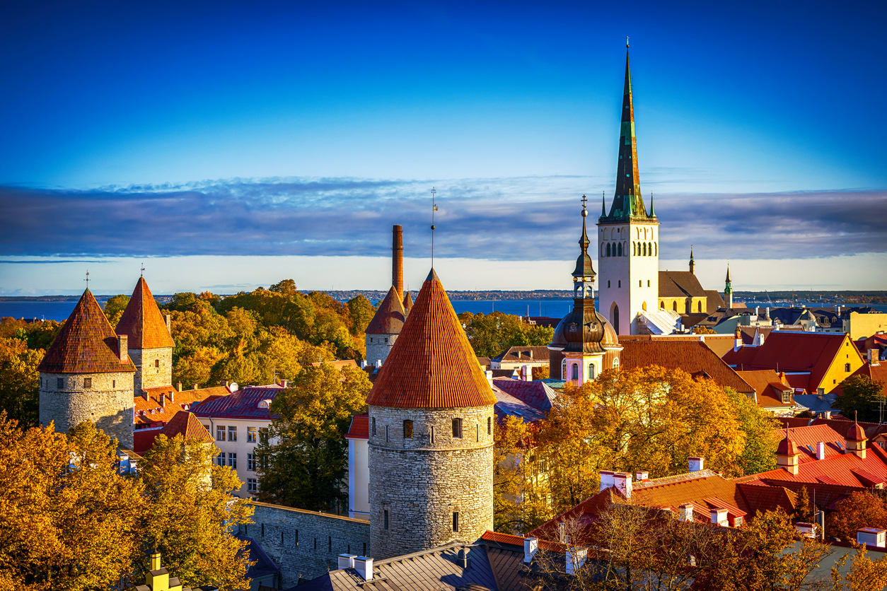 Herbstpanorama von Tallinn mit Stadtmauer-Türmen, Olaikirche und Ostsee im Hintergrund.