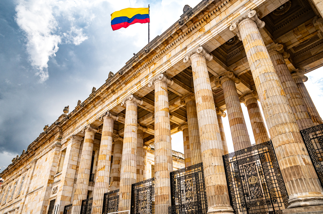 Klassizistisches Kapitolgebäude in Bogotá, Kolumbien, mit markanten Säulen und wehender Nationalflagge vor dramatischem Himmel.