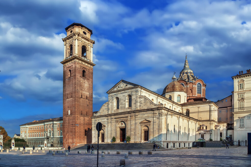 Frontansicht des Turiner Doms (Cattedrale di San Giovanni Battista) mit rotem Glockenturm und Kuppel der Cappella della Sindone unter dramatischem Himmel.