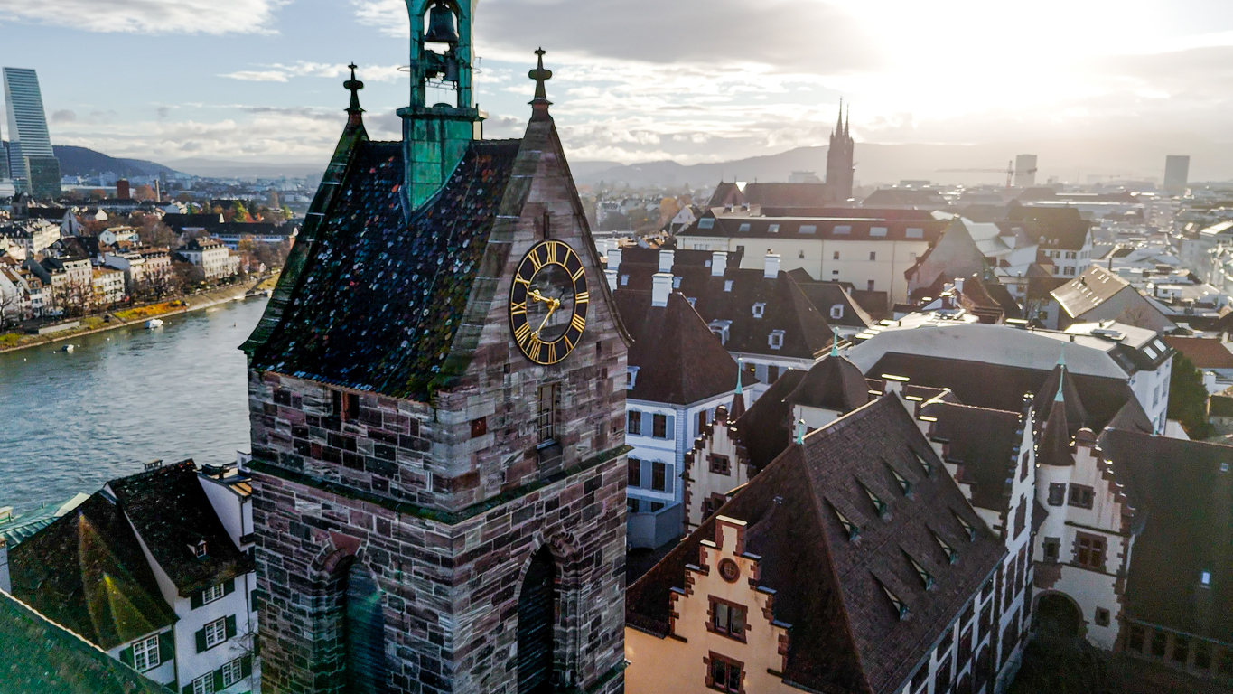 Basel aus der Vogelperspektive mit Uhrturm im Vordergrund, Rhein links, Roche-Turm und Basler Münster in der Ferne im Gegenlicht