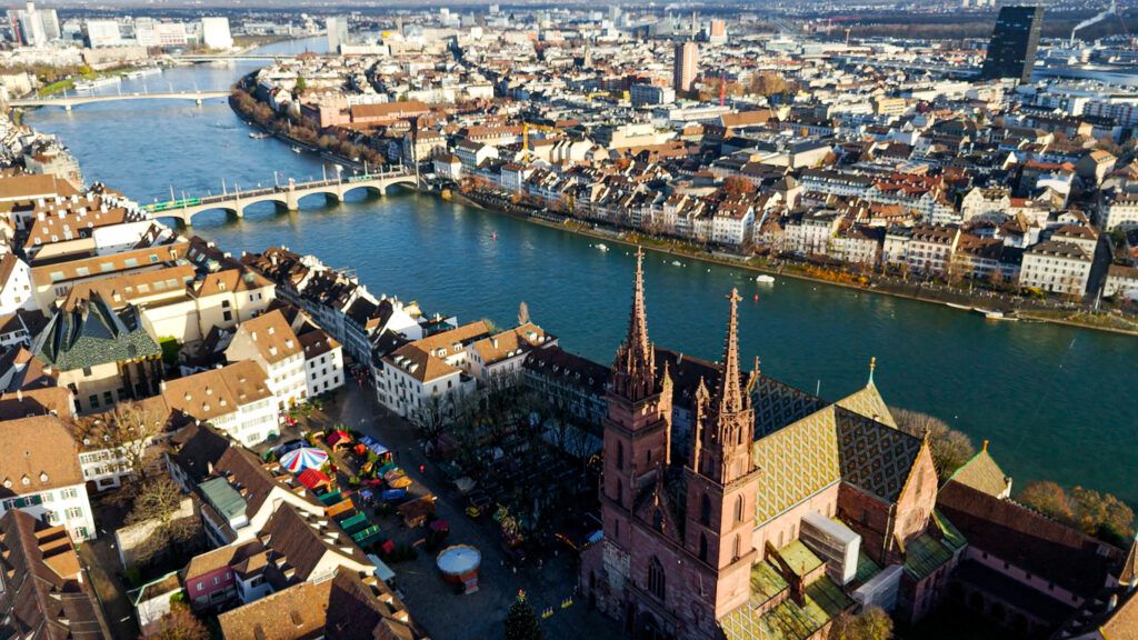 Basel von oben mit Basler Münster im Vordergrund, Rhein mit Brücken und Altstadthäusern, Marktstände auf dem Münsterplatz
