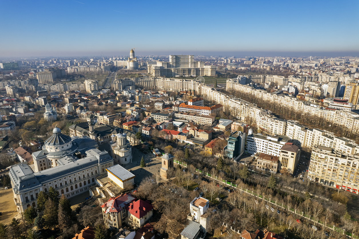 Luftaufnahme von Bukarest mit dem Parlamentsgebäude im Hintergrund und historischer sowie moderner Architektur im Vordergrund.
