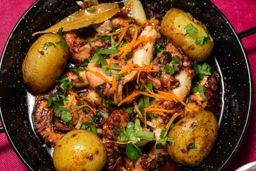 Polvo à Lagareiro – gebackener Oktopus mit kleinen Ofenkartoffeln, Knoblauch, Lorbeer und Petersilie in einer schwarzen Pfanne