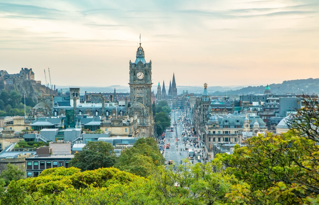 Edinburgh, Blick von Calton Hill über Princes Street mit dem Balmoral-Uhrturm in der Mitte, dichter Stadtverkehr und Dächer der New Town, links Edinburgh Castle, weiches Abendlicht