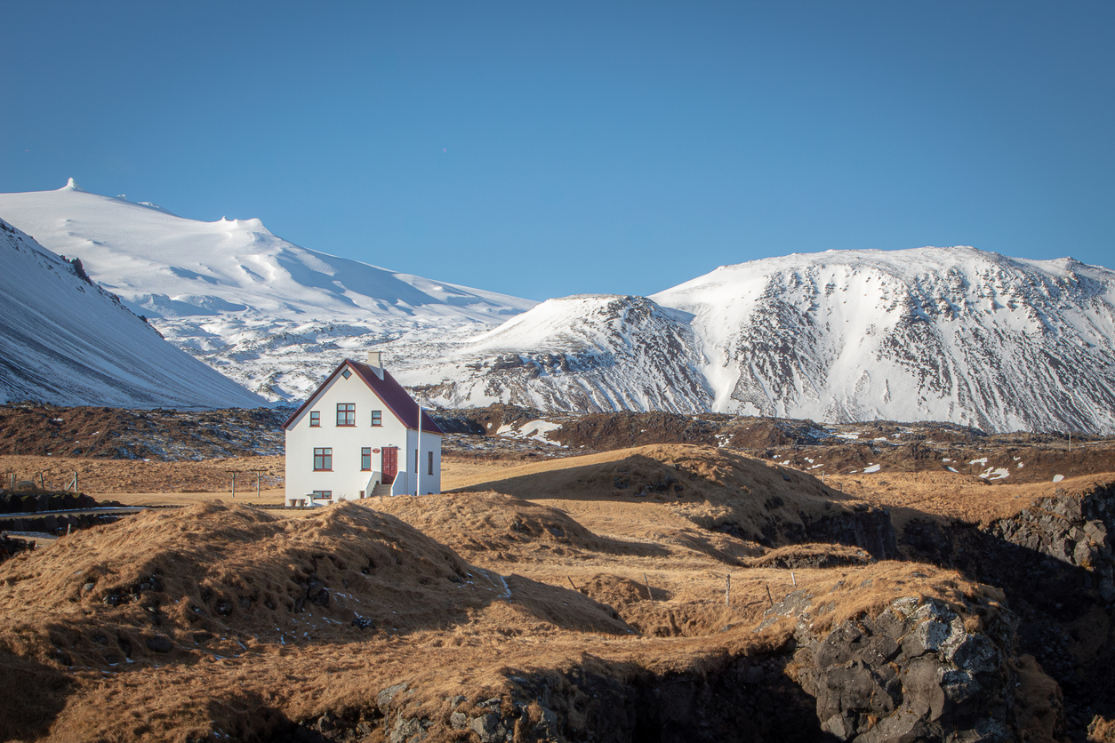 Weißes Haus in isländischer Tundra vor schneebedeckten Bergen auf der Halbinsel Snæfellsnes.