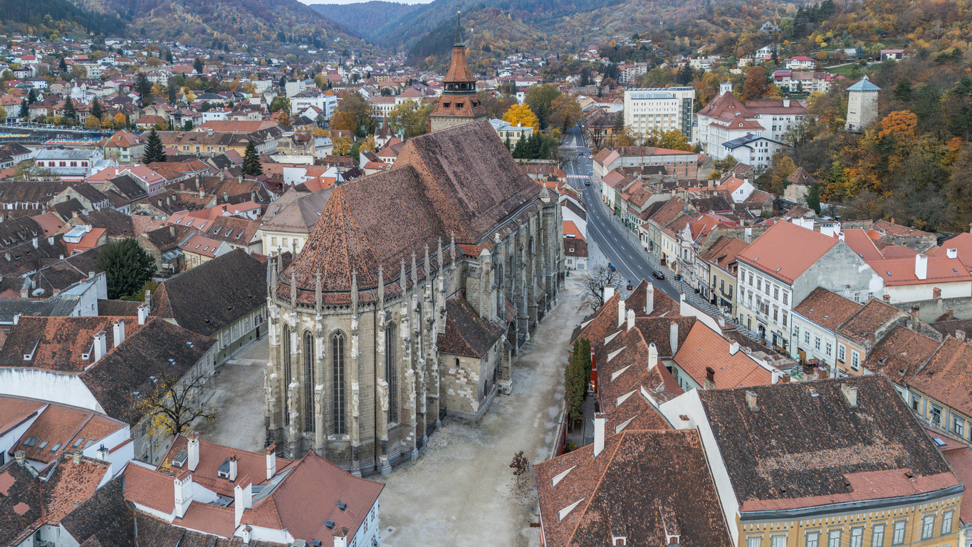 Luftaufnahme der Schwarzen Kirche in Brașov, Rumänien, mit umliegenden historischen Gebäuden und Bergen im Hintergrund.