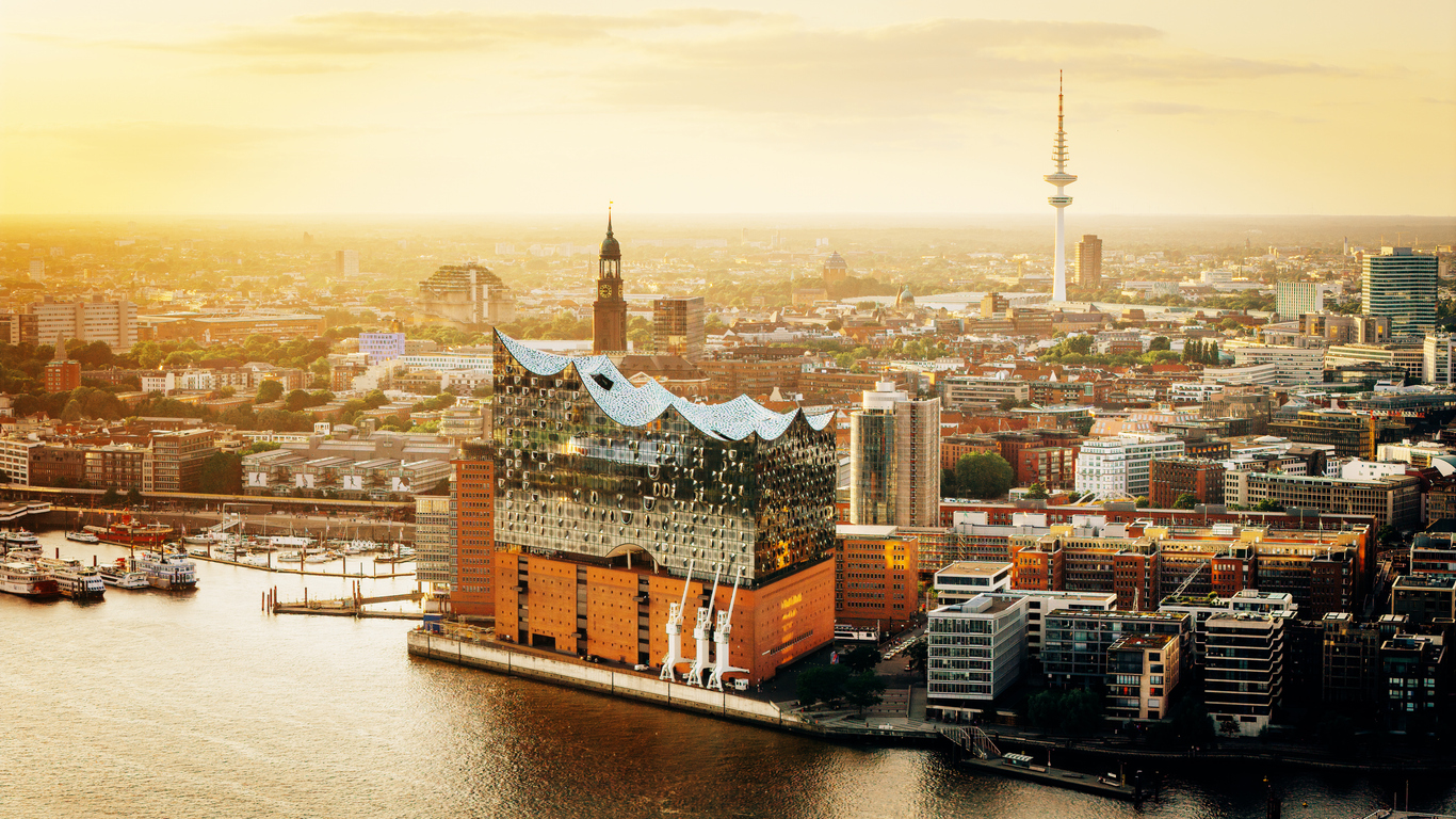 Hamburg, Luftaufnahme der Elbphilharmonie an der Elbe mit gläsernem Wellendach im goldenen Abendlicht, dahinter Innenstadt mit St.-Michaelis-Kirche und Heinrich-Hertz-Turm