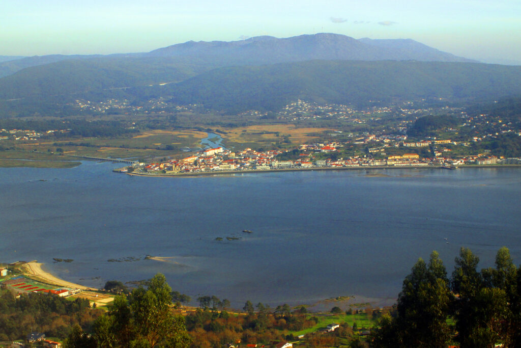 Blick auf den Fluss Minho mit Uferstadt, Brücke und Bergen im Hintergrund.