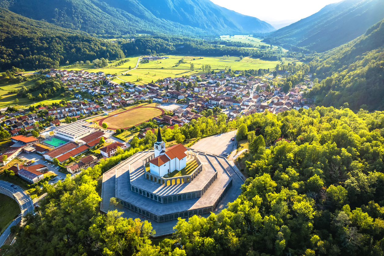 Aerial von Kobarid mit oktogonalem Ossarium und Kirche über der Stadt, umgeben von Grünflächen und Bergkulisse